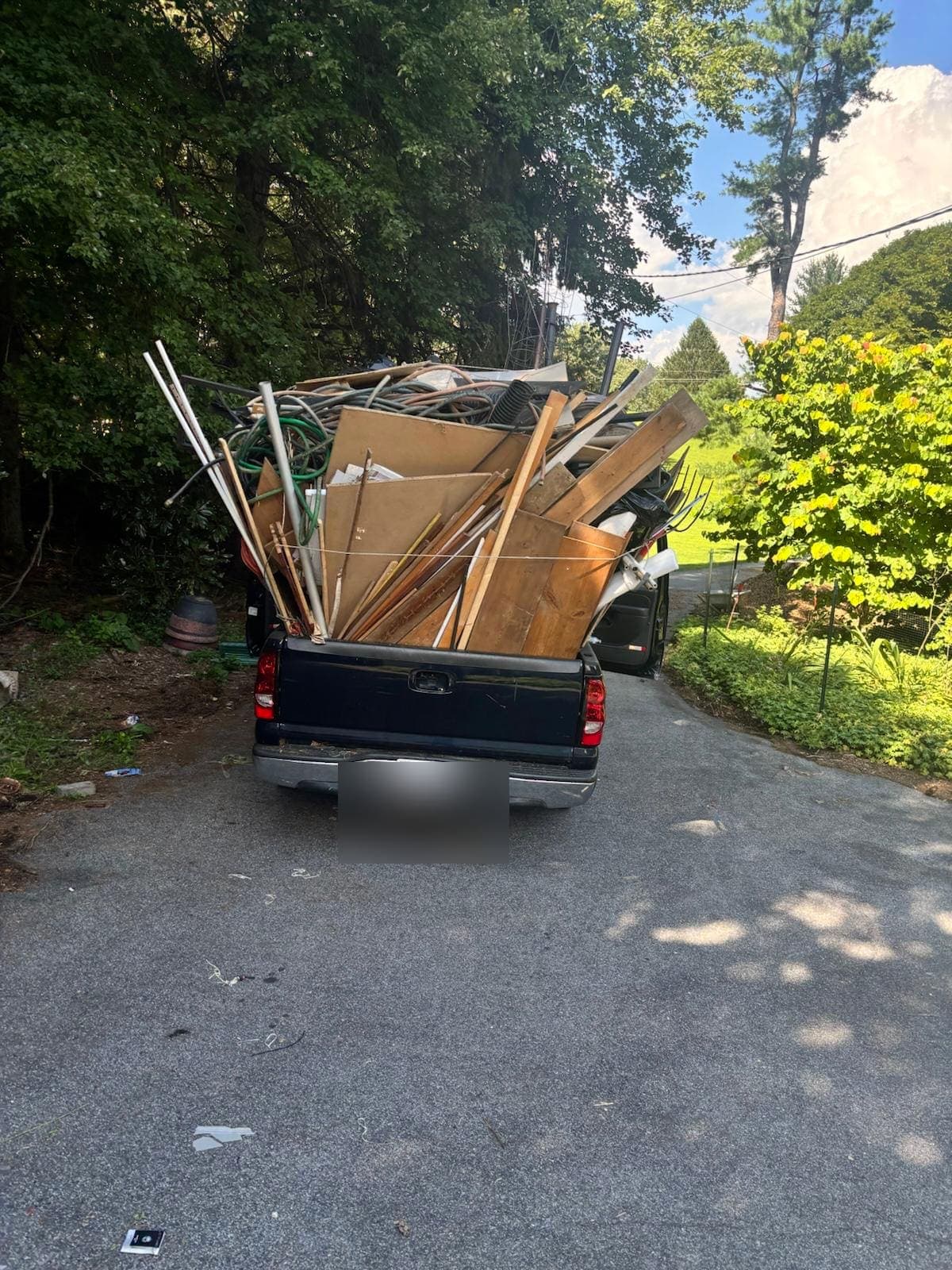 Pickup in a driveway, the bed stacked with boards, hose, and cardboard.
