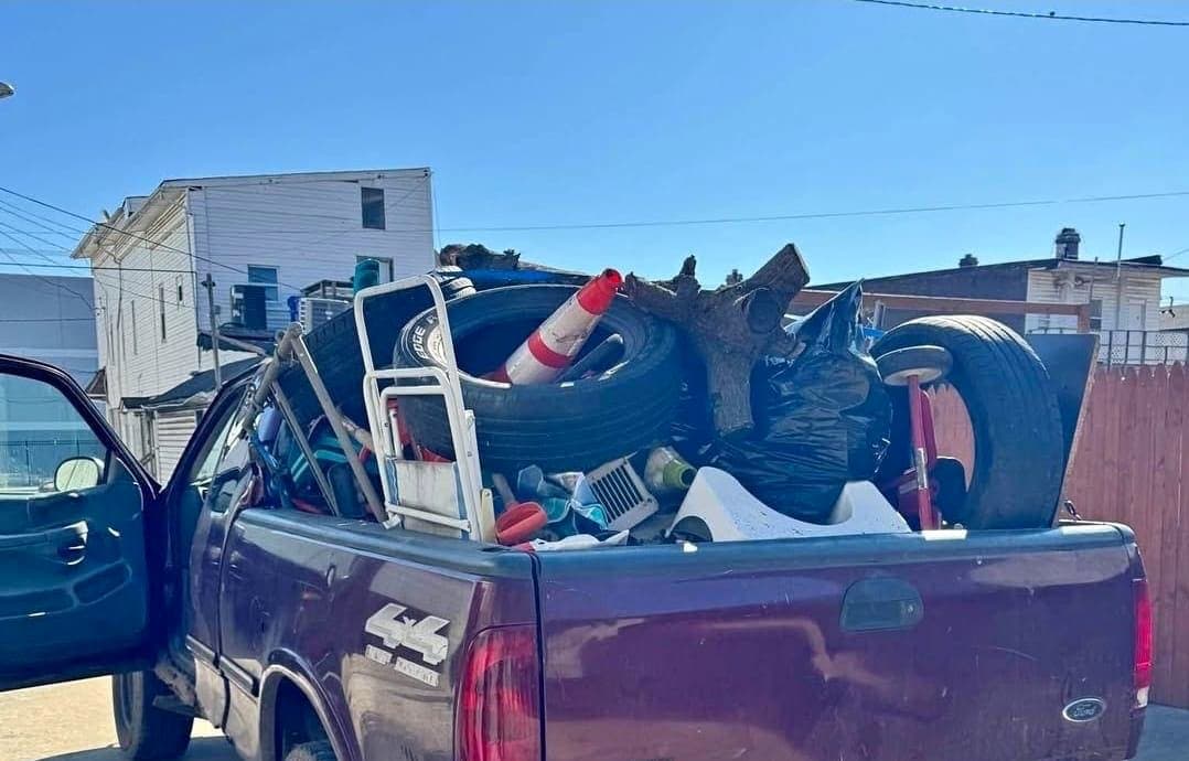Maroon pickup loaded with tires, a traffic cone, a stump, and bagged junk.